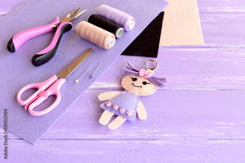Adorable doll keychain, pliers, thread, needle, pins, scissors, felt, cord, hollofayber on wooden background with empty space for text. Supplies for sewing cute character. Crafts for children  photo