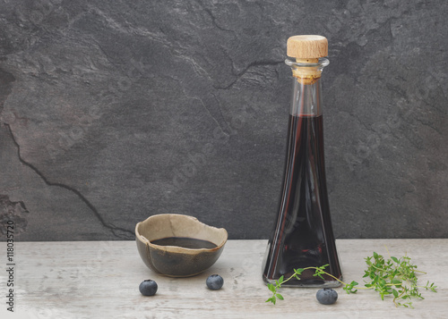 Blueberry vinegar in glass bottle with fresh blueberries and thyme on rustic table. 