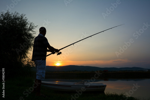 Young man fishing on a lake at sunset