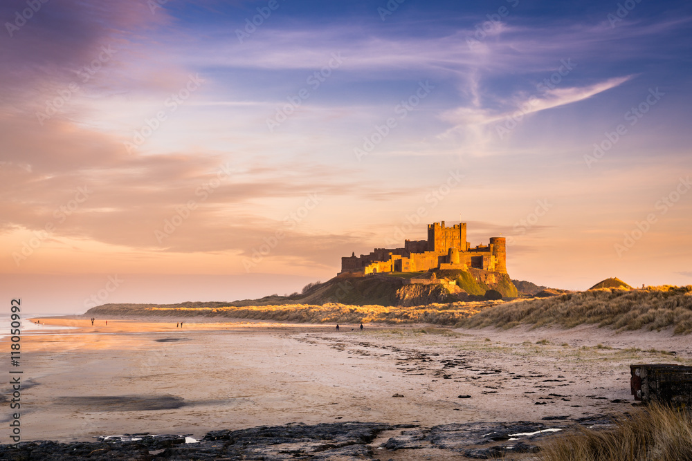 Golden Bamburgh Castle, on the Northumberland coastline, bathed in late afternoon golden sunlight