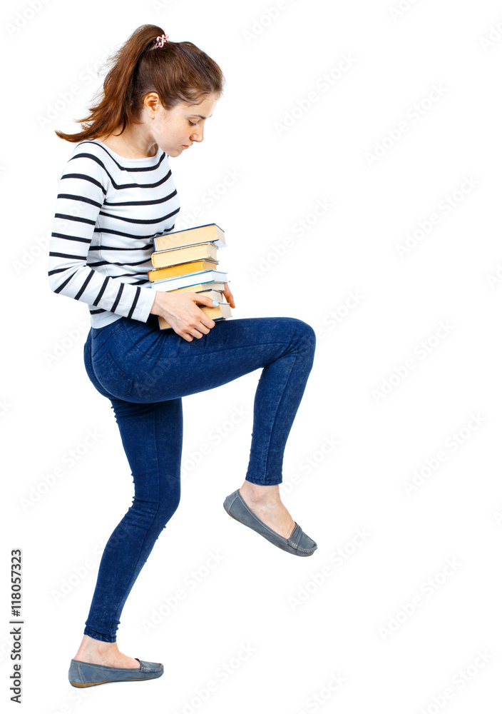 Girl carries a heavy pile of books. back view. Rear view people collection. backside view of person. Isolated over white background. Girl in a striped sweater knee supports books. Girl carries a heavy pile of books. back view. Rear view people collection. backside view of person. Isolated over white background. Girl in a striped sweater knee supports books.
