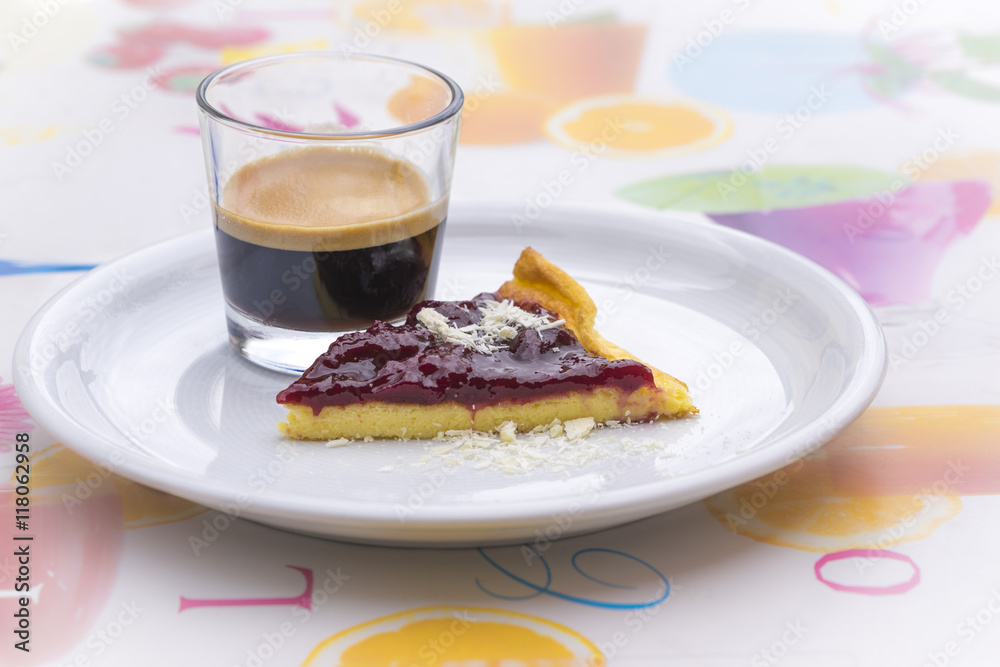 Single round ceramic white plate with espresso and red peach cheesecake wedge over colorful tablecloth Single round ceramic white plate with espresso and red peach cheesecake wedge over colorful tablecloth
