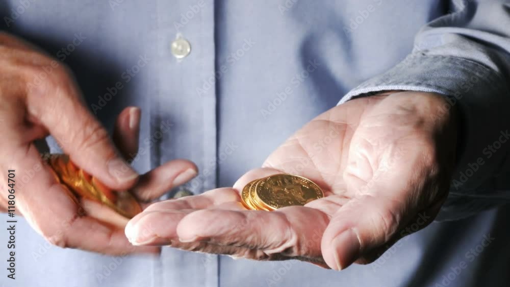 Close view of the hand of senior caucasian adult man counting US Mint gold eagle coins one by one into his hand and then closing his fist around them