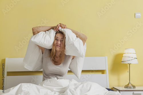 Female sitting on bed and closing her ears with pillow