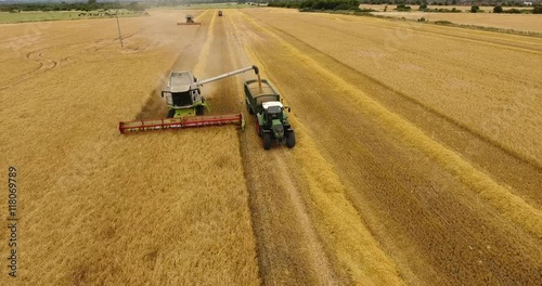 Aerial view flying over the top of a combine harvester and tractor and trailer as it empties the corn in a field on a summers day