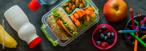 School lunch box with books and pencils in front of black board