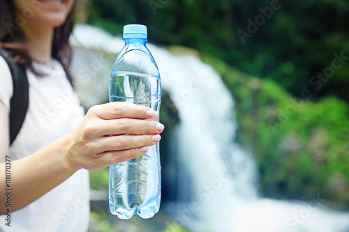 Female tourist holding bottle of clear water on blurred river background photo