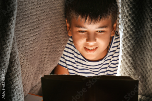 Cute boy reading book at night