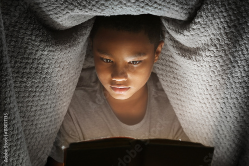 Cute boy reading book at night