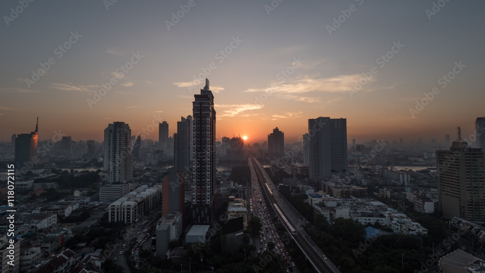 Sunset time in Bangkok, Thailand. City panorama with highrise urban architecture and traffic on highway. Sky in warm colors and sun going down
