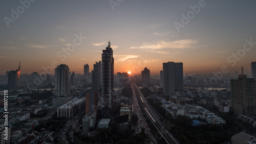 Sunset time in Bangkok, Thailand. City panorama with highrise urban architecture and traffic on highway. Sky in warm colors and sun going down