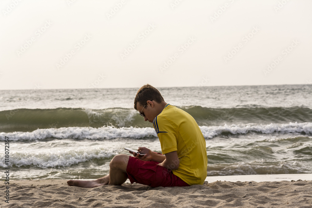 teenager with the phone sitting on the beach teenager with the phone sitting on the beach