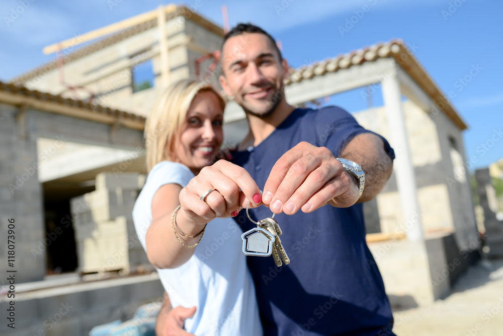 cheerful young happy couple holding home keys in front of contruction ...