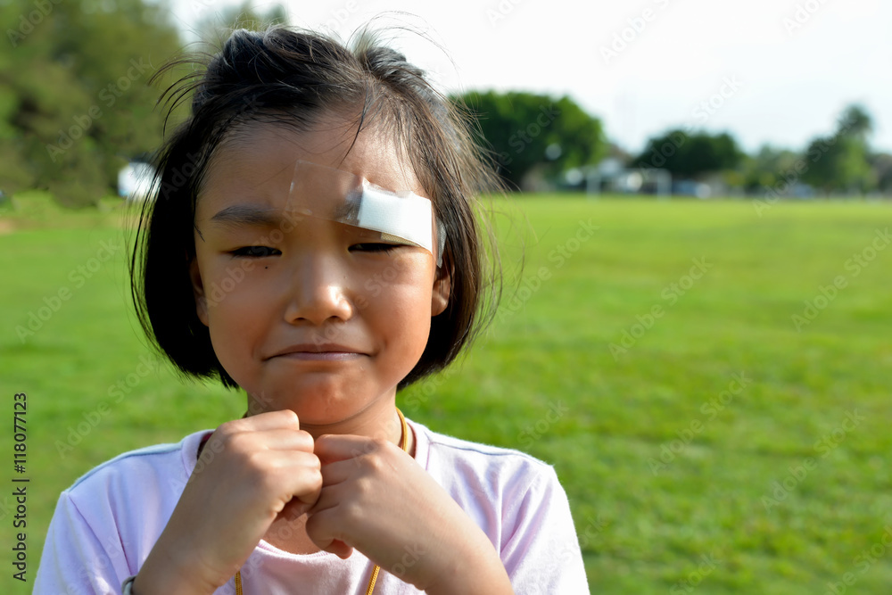 Little cute girl with plaster on eyebrows,girl hurt and cry at green field Little cute girl with plaster on eyebrows,girl hurt and cry at green field