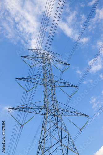 Electricity pylon silhouetted against blue sky wih cloud background. High voltage tower