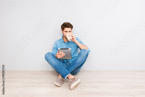 Young man sitting on floor with crossed legs and tablet and drin