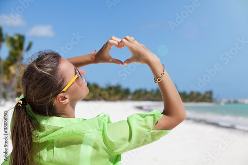 Woman standing on white sand making a hart shape with fingers.