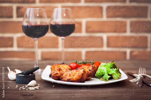 Juicy pieces of grilled meat fillet served with cherry tomatoes branch and lettuce on a white plate  glass of red wine  knife  fork  on the brick wall background. Romantic concept. Horizontal