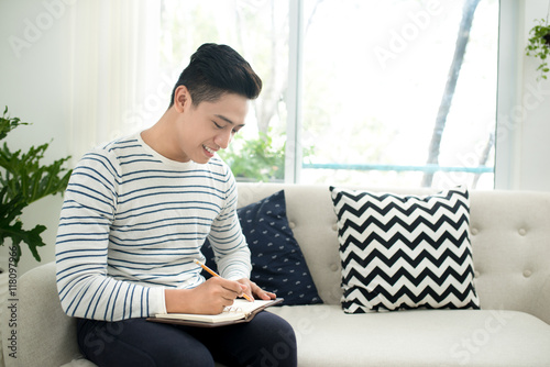 Handsome young man at home writing writing down thoughts in jou