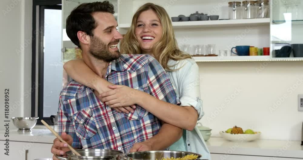 Cute girl hugging his boyfriend while he is cooking food in the kitchen Cute girl hugging his boyfriend while he is cooking food in the kitchen