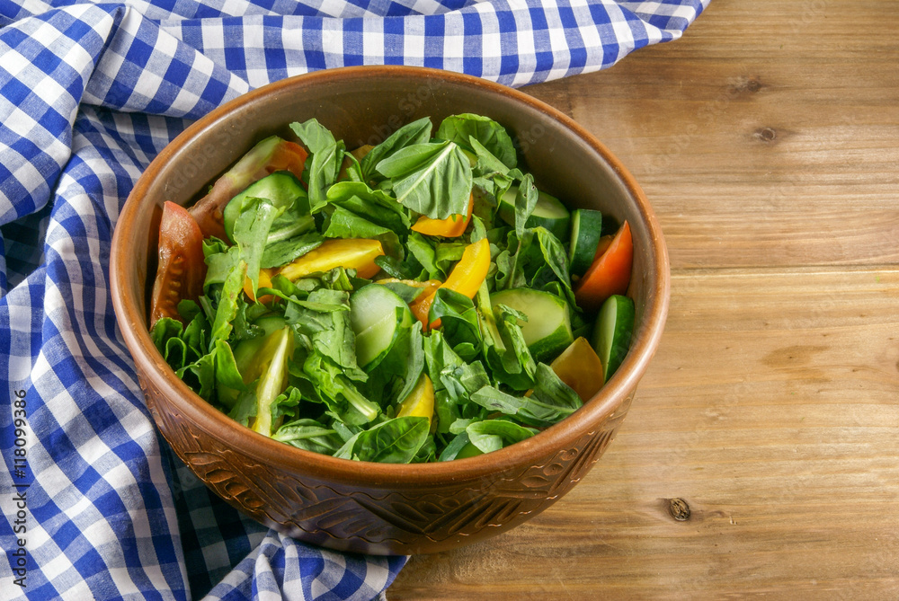 A large portion of salad with fresh basil leaves, arugula, parsley, tomatoes. On a wooden table with a tablecloth. Copy space A large portion of salad with fresh basil leaves, arugula, parsley, tomatoes. On a wooden table with a tablecloth. Copy space