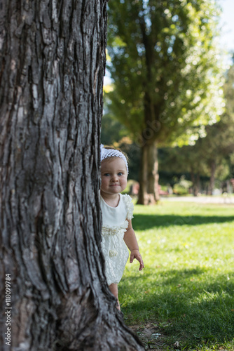 Portrait of happy little girl looking at camera while hiding behind tree trunk