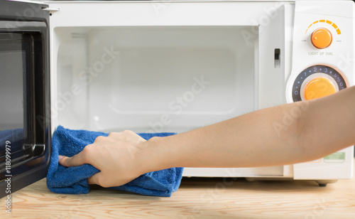 Close up woman hand with microfiber cleaning rag wiping microwave oven.