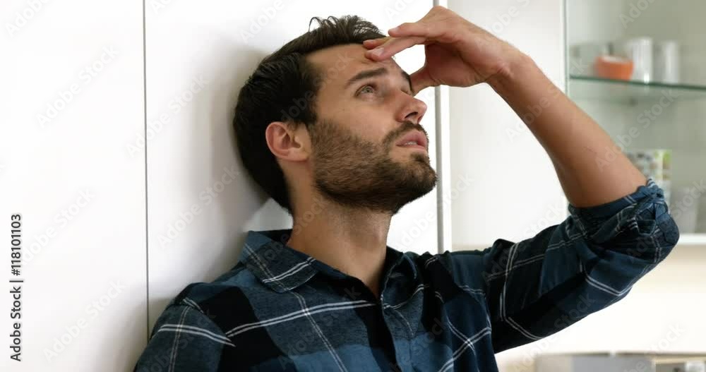 Man is standing against a wall with a sad expression on his face at home Man is standing against a wall with a sad expression on his face at home