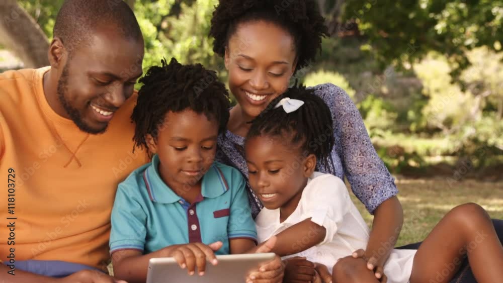 Family is sitting on the grass and looking a tablet Family is sitting on the grass and looking a tablet