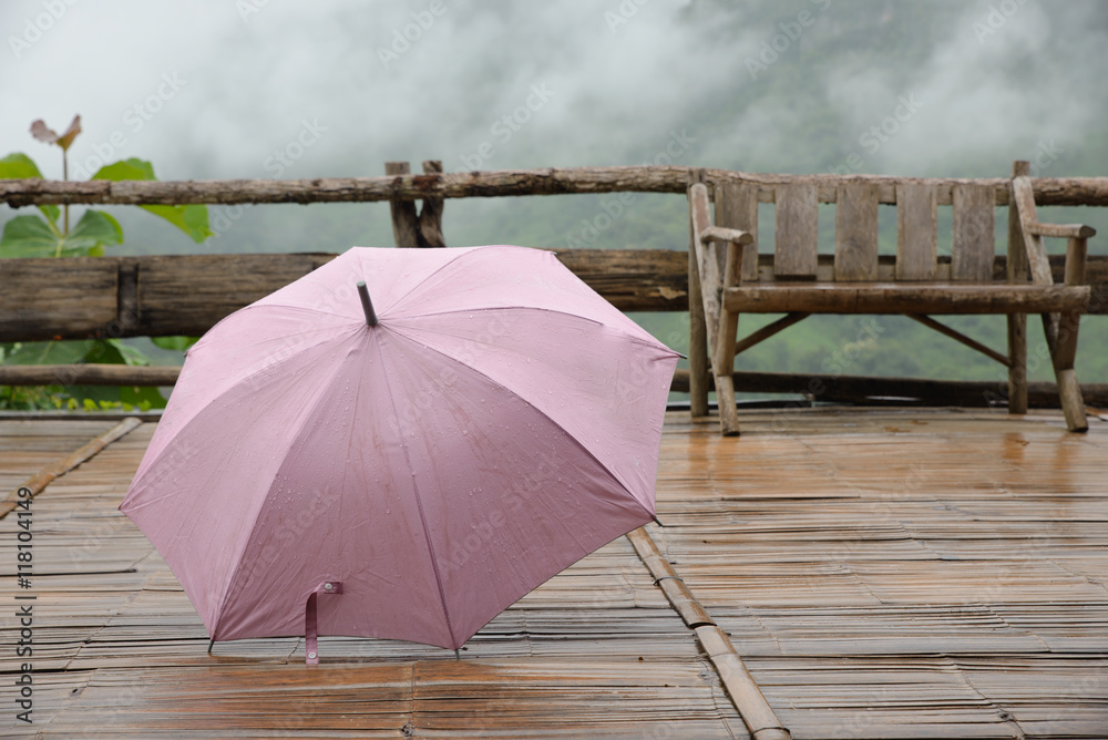 Pink umbrella on wet wood terrace,mountain and fog background,rainy day.