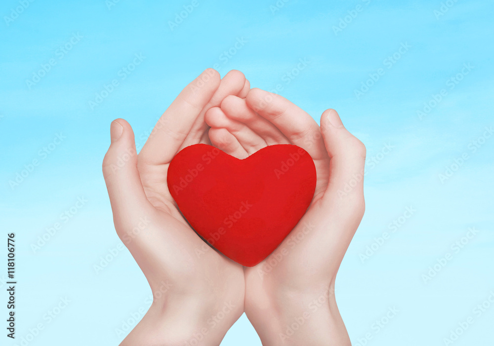 Open hands holding showing red heart over blue sky background Open hands holding showing red heart over blue sky background