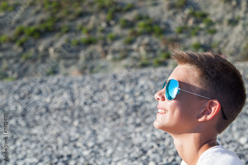 Подросток сидит на пляже в голубой очки от солнца