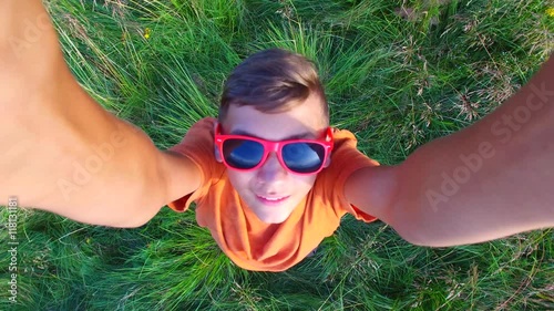 Aerial view of a boy in a red sunglasses having fun in a mountain meadow. Smiling boy is playing with drone.