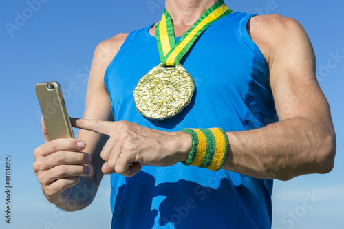 Brazilian gold medal athlete with green and yellow Brazil color wristbands using mobile phone against blue sky