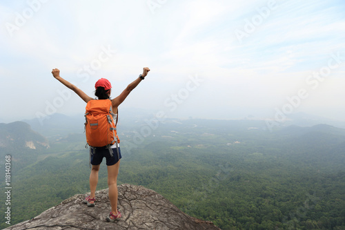 cheering successful woman backpacker open arms on mountain peak
