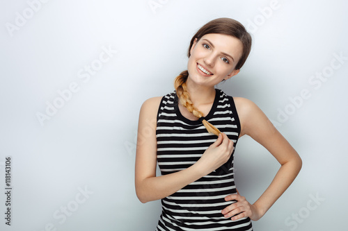 Portrait of happy young beautiful woman in striped shirt touching her hair braid posing for model tests against studio background