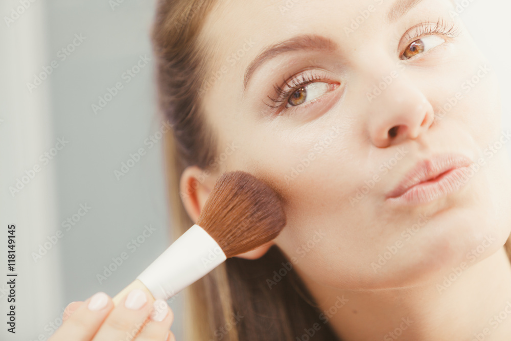 Woman applying bronzing powder with brush to her skin Woman applying bronzing powder with brush to her skin