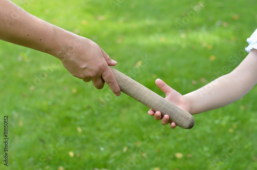 woman giving the relay baton to the next generation into a child's hand