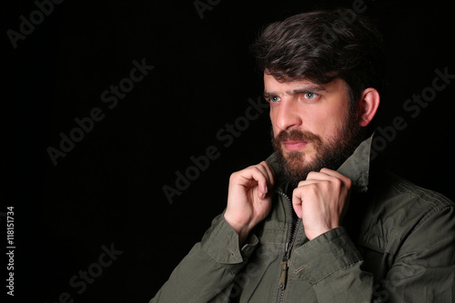 Bearded man in khaki jacket holding his collar. Close.up. Black