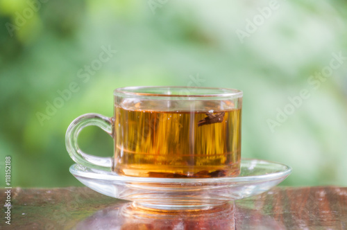 Hot tea cup on wooden table with green nature background, tea time concept