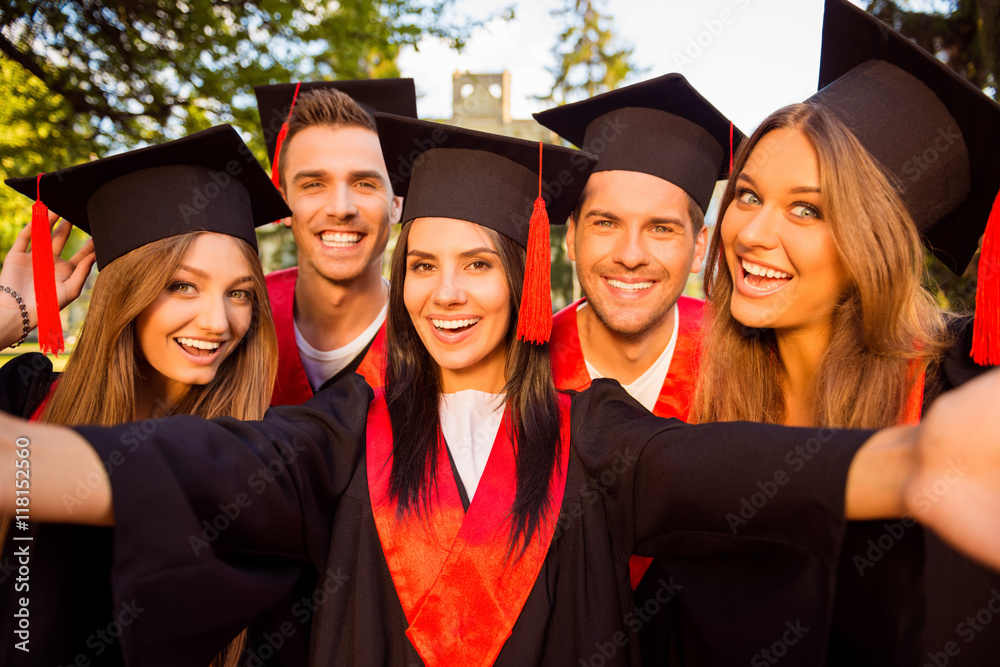 Fototapeta premium excited five successful happy five graduates in robes and hats w
