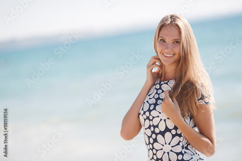 Portrait of happy woman on the beach,brunette with long hair and gray eyes,a beautiful smile and white straight teeth,wearing a black dress with large white daisies
