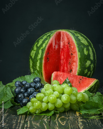 Fototapeta Naklejka Na Ścianę i Meble -  Sliced watermelon, red and green grapes on a wooden table