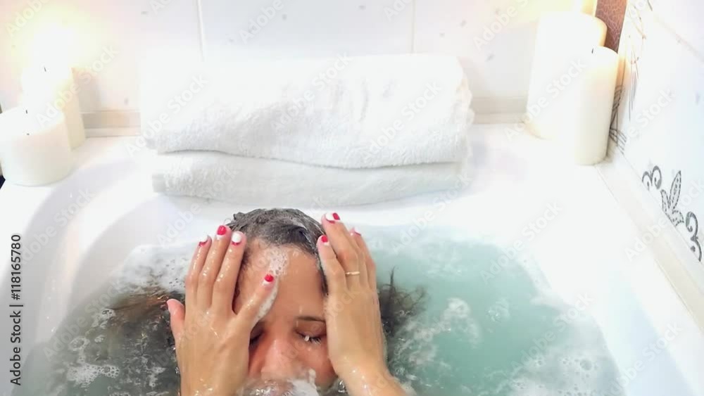 Young beautiful woman relaxing in a bath, washing herself hair and face