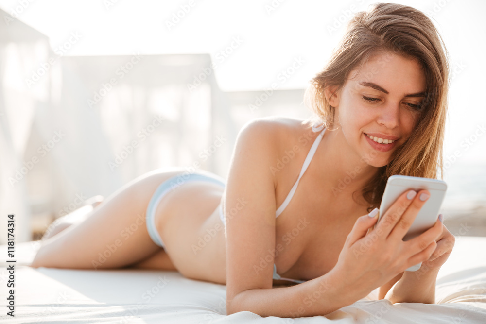 Portrait of a girl in bikini lying and using smartphone Portrait of a girl in bikini lying and using smartphone
