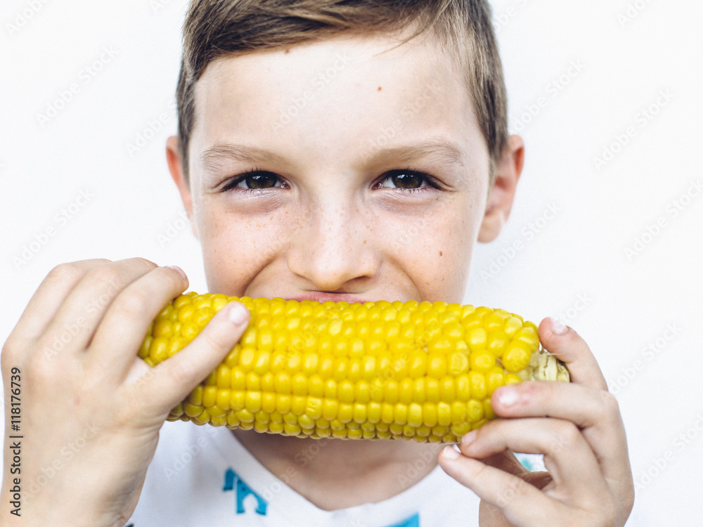Preteen boy with smiling eyes holding in hands and biting into bright yellow sweetcorn Preteen boy with smiling eyes holding in hands and biting into bright yellow sweetcorn