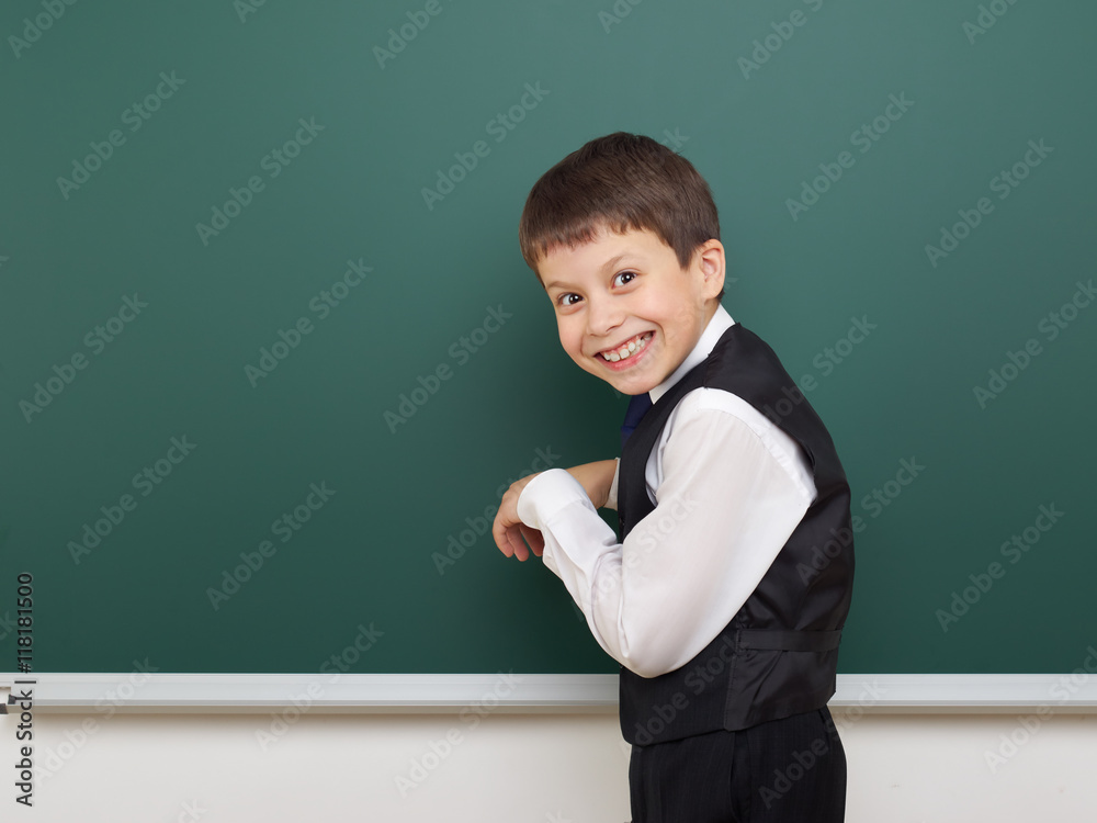 school student boy posing at the clean blackboard, grimacing and emotions, dressed in a black suit, education concept, studio photo