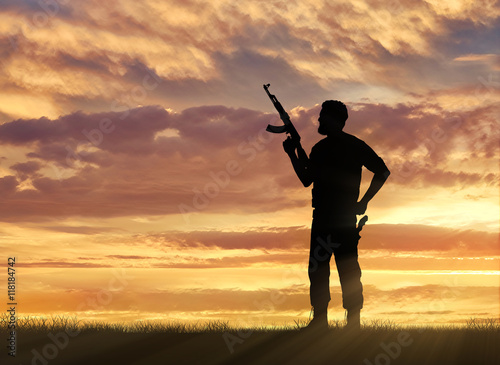 Silhouette of man with rifle standing against cloudy sky during sunset