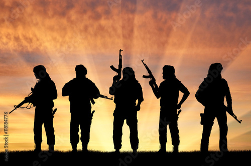 Silhouette of men with rifles standing against cloudy sky during sunset