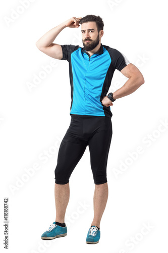 Puzzled young cyclist in sports clothes scratching head looking at camera. Full body length portrait isolated over white studio background.
